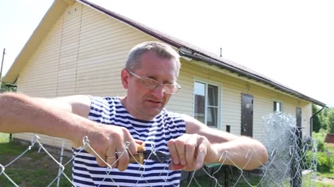 Installing chain-link fence in local area, homeowner braids ends of wire so.. Stock Footage 277302797