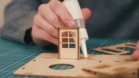 Installing first wall with glue in wooden miniature house assembly. DIY Stock Footage 336309784