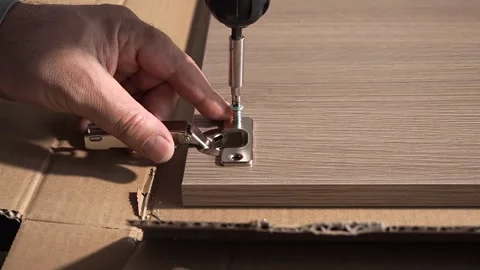 Installing hinges on a furniture door using an electric screwdriver. Stock Footage 253480683