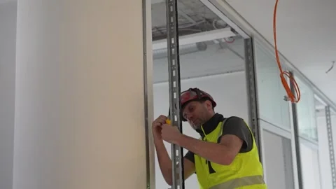 Installing metal stud wall frame in drywall construction, worker fixing Stock Footage 332584302