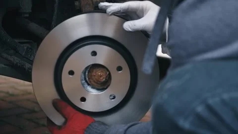 Installing new brake disc onto wheel hub during replacement process. DIY Stock Footage 340195440