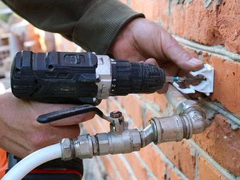 Installing plumbing fasteners into a brick wall using a power screwdriver. Stock Photos