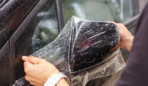 Installing PPF on the mirror of the car. Stock Photos
