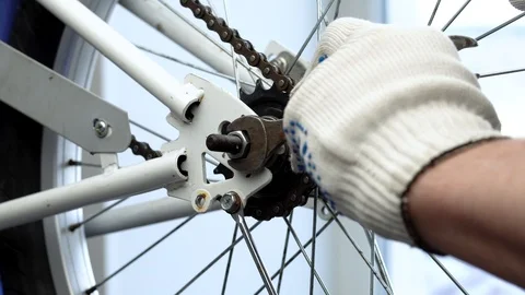 Installing the rear wheel in the bike frame. A repairman in white gloves fixes a Stock Footage 117800883