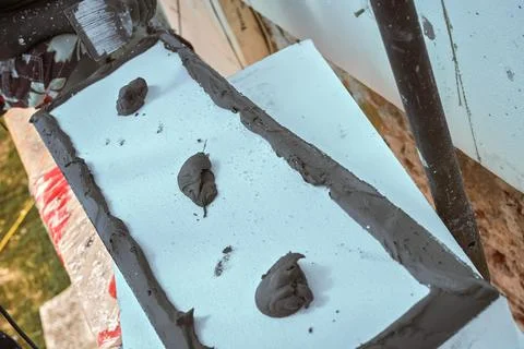 Installing white polystyrene heat insulation, detail on gray bonding cement.. Stock Photos