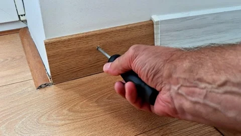 Installing a Wooden Baseboard with a Screwdriver During Floor Repair Work Stock Footage 345703756