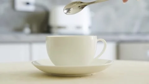 Instant black coffee is poured from a spoon into a white cup in a home interior Stock Footage 154708586