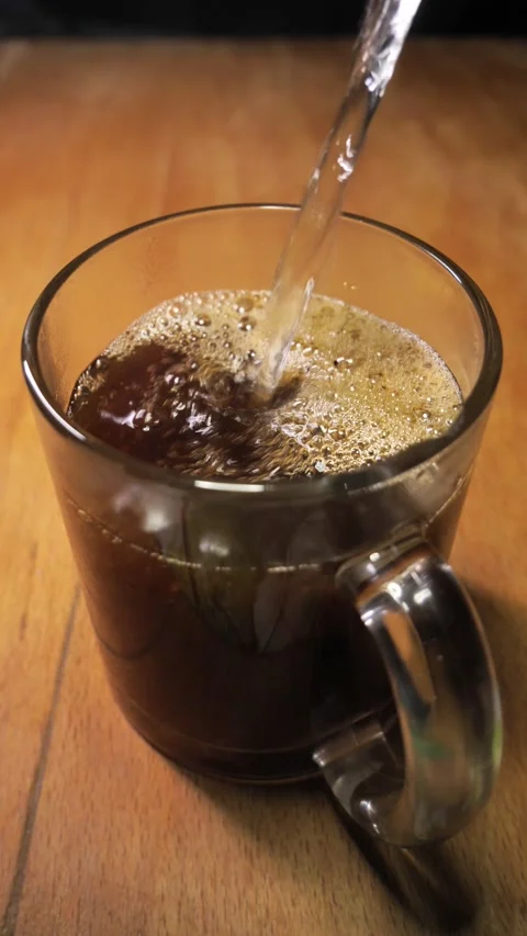 Instant coffee is poured with boiling water into a glass cup. coffee foam Stock Footage 293066142