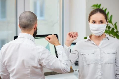 Instead of greeting with a hug a man and a woman with a face mask bump elbows Stock Photos