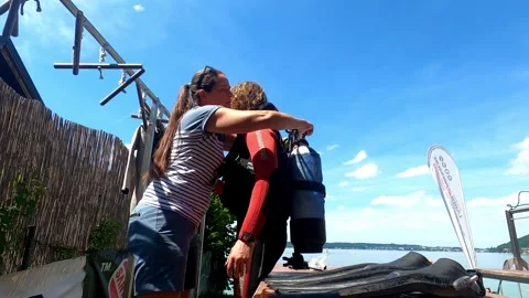 Instructor assisting scuba student with gear setup and safety check at lakeside Vídeo Stock 330970535