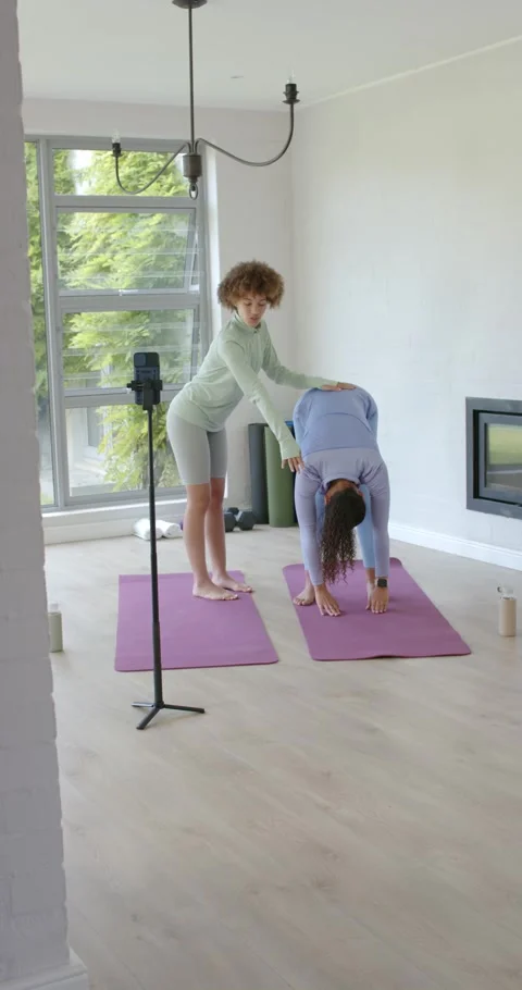 Instructor checking phone, placing hands and guiding client deepening fold for Stock Footage 346724042