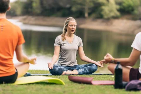 Instructor doing the lotus pose during a yoga class in a park Stock Photos