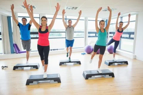 Instructor with fitness class performing step aerobics exercise Stock Photos