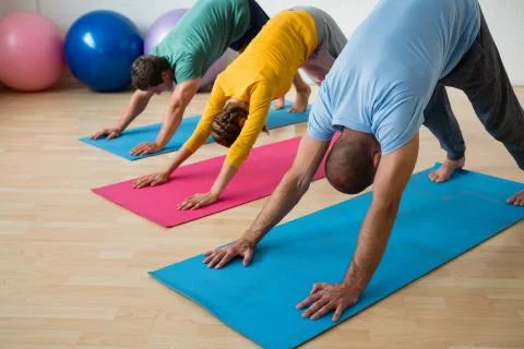 Instructor guiding students in practicing downward facing dog pose at yoga Stock Photos