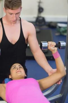 Instructor helping lying brunette exercising with dumbbells 写真素材