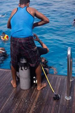 The instructor helps the tourist to put on a diving suit. vertical Stock Photos