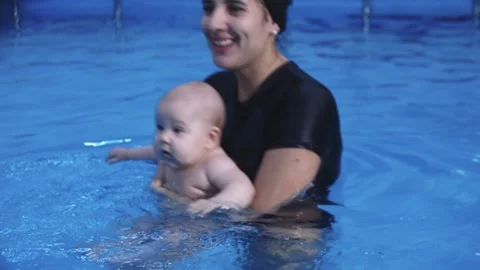 Instructor holding baby while teaching infant to swim in pool Stock Footage 310241908