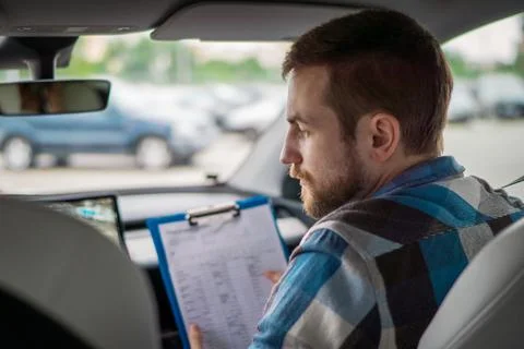 Instructor holding drive test report while sitting on the passenger seat. Back Stock Photos