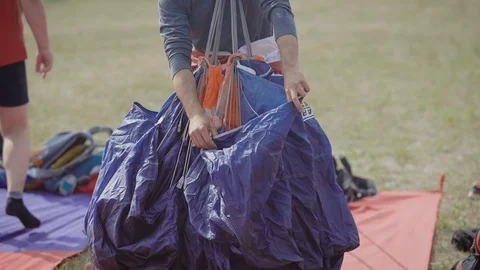 Instructor is packing parachute canopy before a flight in open area in summer Stock Footage 95099871