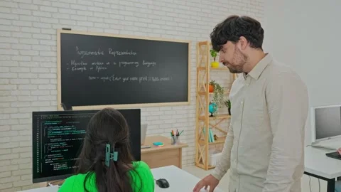 Instructor Providing One-on-One Coding Assistance in Classroom Stock Footage 281072534
