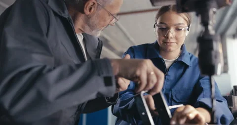 Instructor showing apprentice how to measure metal parts in workshop Video stock 254676421