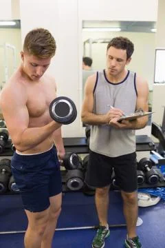 Instructor taking notes of handsome man lifting dumbbells Stock Photos