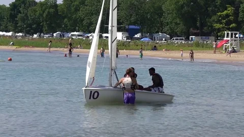 INSTRUCTOR IN WATER TALKING WITH TWO STUDENTS IN A SMALL SAILBOAT Stock Footage 78874834
