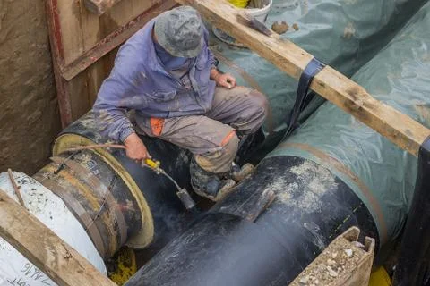 Insulation worker applied tar coating on underground heating pipe Stock Photos