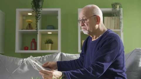Intellectual old man sitting on sofa at home and reading news Stock Footage 232241781