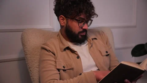 Intelligent bearded man reading a book in an armchair Video stock 346989402