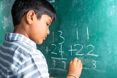 Intelligent elementary school kid solving maths problem on chalkboard at Stock Photos