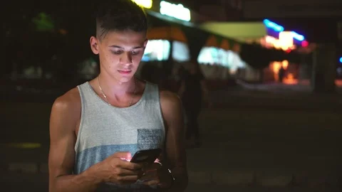 Intelligent young man browsing the net on his phone in a city street at night in Stock-Footage 100577816