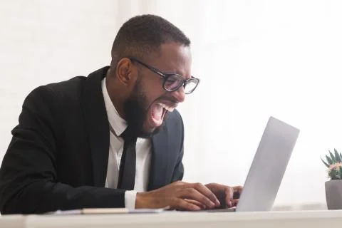 Intense black manager using laptop and screaming at workplace Фото