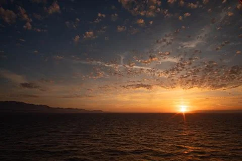 Intense evening sky with glowing cloudscape, ripples on ocean and distant i.. Stock-Fotos