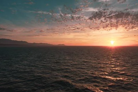 Intense sunset sky with whispy clouds over gentle ocean Stock Photos