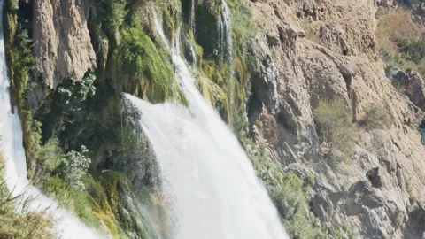 Intense water flow falls from a high rocky ridge adorned with patches of gre 動画素材 333741244