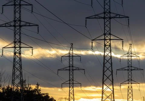 Interconnected Web of Electrical Towers Against a Sunset Sky Foto stock