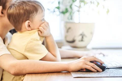 Interested boy looks into computer sitting on brother knees Stock Photos