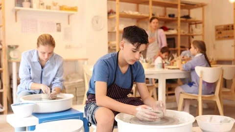 Interested children of different ages working at potters wheel with teacher in Stock Footage 317531242