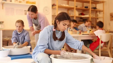 Interested children of different ages working at potters wheel with teacher in Stock Footage 327140312