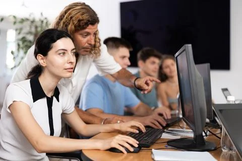 Interested girl attending computer class under guidance of male teacher Stock-Fotos