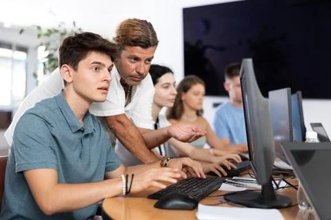 Interested guy attending computer class under guidance of male teacher Fotos de archivo