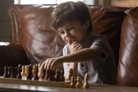 Interested small adorable child boy playing chess alone at home. Stock Photos