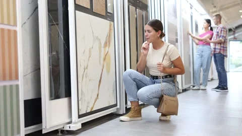 Interested young female customer browsing tile samples on display stand in home Stock Footage 310069387