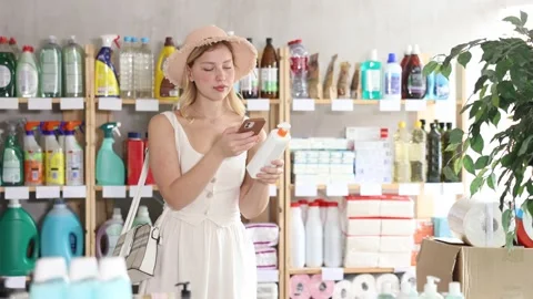 Interested young female shopper scanning barcode on bottle of tanning lotion Stock Footage 344844580