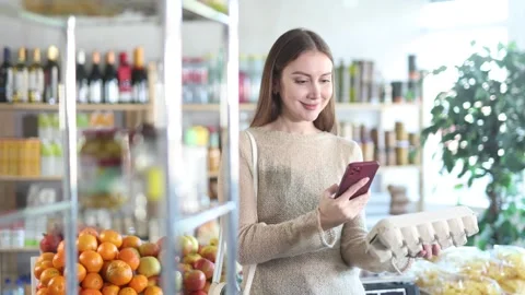 Interested young woman scanning barcode on egg carton with phone while shopping Stock Footage 329396996