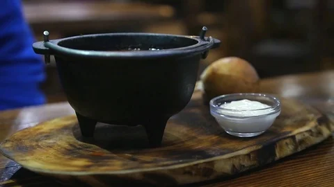 Interesting serving of a dish, red soup in a cast iron plate on a wooden board Stock Footage 82991887