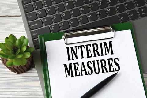 INTERIM MEASURES - words on a white sheet on the background of a laptop and.. Stock Photos