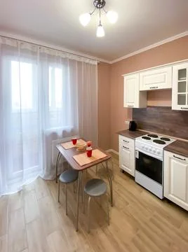 Interior of a beige kitchen with a white kitchen set and a stove, a table wit Photos