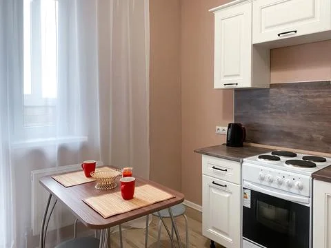 Interior of a beige kitchen with a white kitchen set and a stove, a table wit Stock Photos